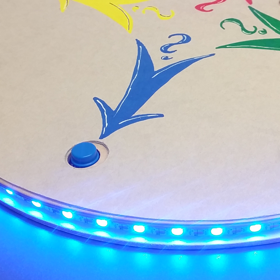 Foto einer Leuchtscheibe: blau leuchtende LEDs und blaue 
                        Taste mit blauem Pfeil auf Buzzer-Spielfeld