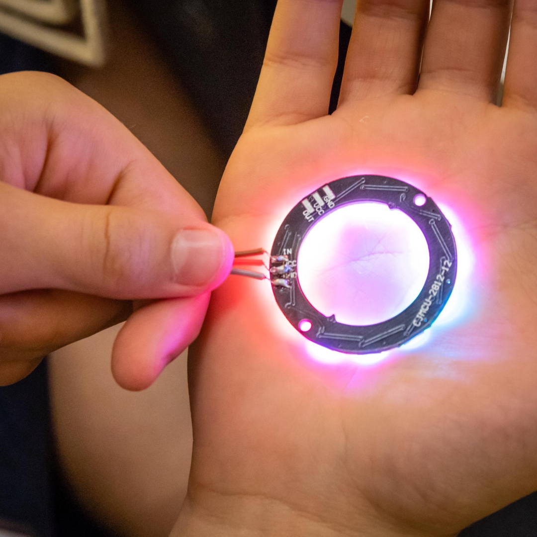Foto eines Bauteils der Leuchtscheibe-mini: rosa leuchtender LED-Ring in der Hand gehalten